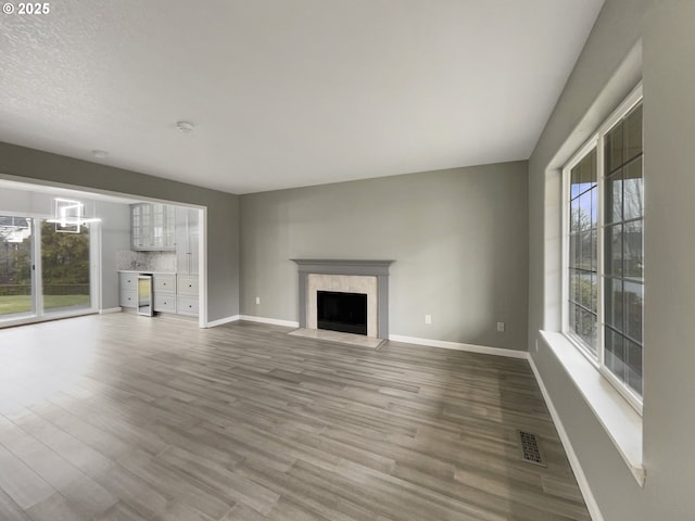 unfurnished living room featuring a premium fireplace, wood finished floors, visible vents, and baseboards