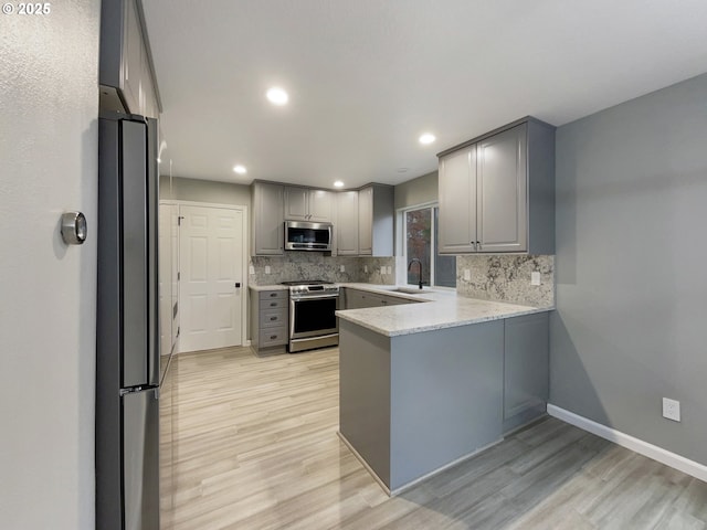 kitchen with stainless steel appliances, backsplash, light wood-style flooring, gray cabinetry, and a peninsula