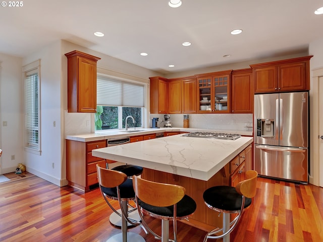 kitchen with light stone countertops, a center island, stainless steel appliances, light hardwood / wood-style floors, and a breakfast bar area