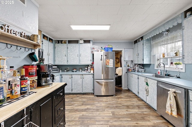 kitchen with appliances with stainless steel finishes, a sink, light countertops, dark cabinetry, and light wood-style floors