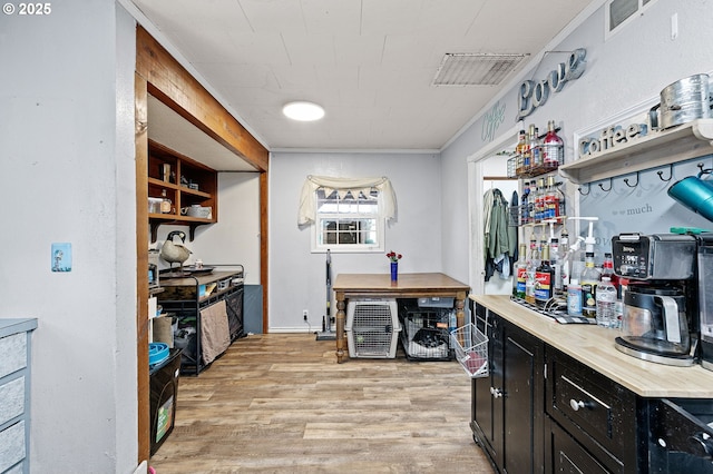 kitchen featuring dark cabinets, light wood-style floors, crown molding, light countertops, and open shelves