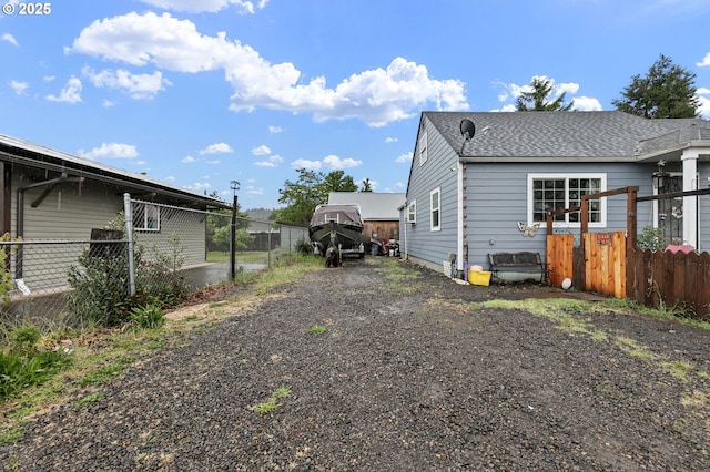 view of property exterior with gravel driveway, fence, and roof with shingles