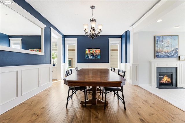 dining area featuring an inviting chandelier, wainscoting, a decorative wall, hardwood / wood-style flooring, and a tiled fireplace