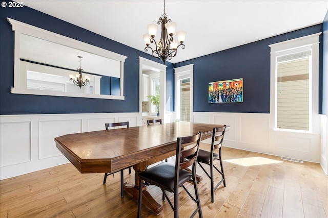 dining space featuring visible vents, wainscoting, light wood-type flooring, a notable chandelier, and a decorative wall