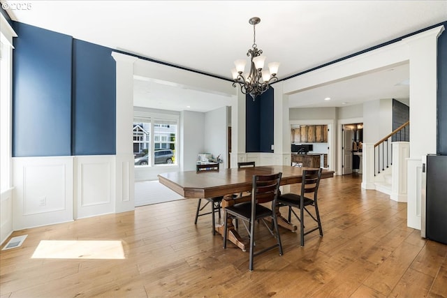 dining room featuring a decorative wall, visible vents, wainscoting, and a notable chandelier