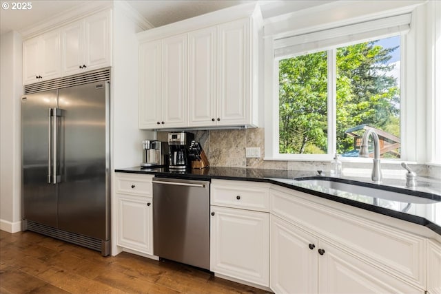 kitchen with decorative backsplash, dark wood-style flooring, a sink, stainless steel appliances, and white cabinetry