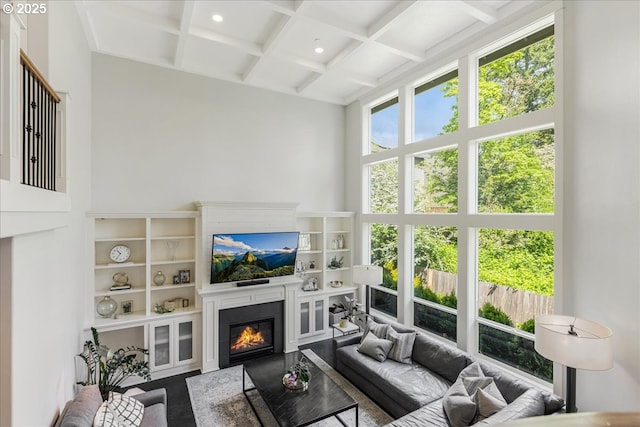 living area with beamed ceiling, a glass covered fireplace, a high ceiling, coffered ceiling, and recessed lighting