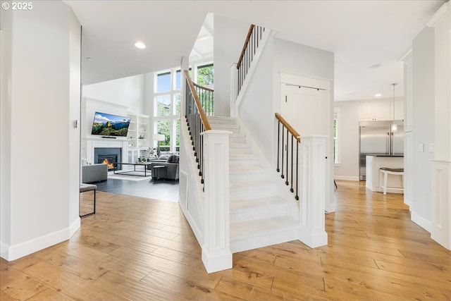 stairway with recessed lighting, a warm lit fireplace, and hardwood / wood-style flooring
