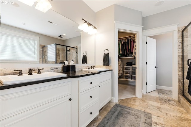 bathroom with double vanity, a walk in closet, a sink, and a stall shower