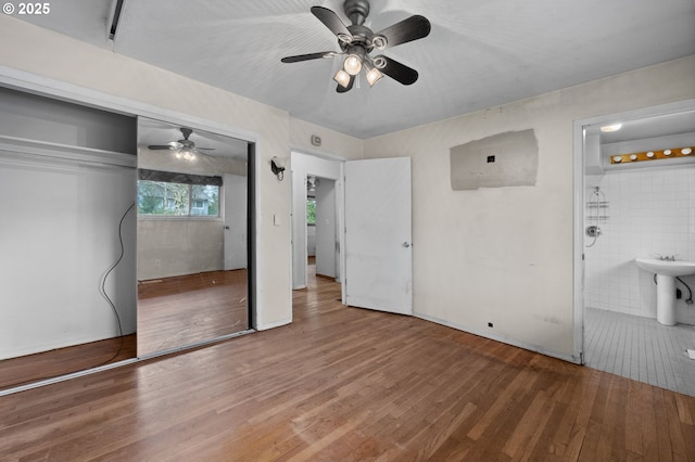 unfurnished bedroom with a closet, ensuite bathroom, ceiling fan, and wood finished floors