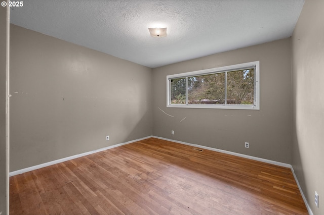 unfurnished room with visible vents, wood finished floors, baseboards, and a textured ceiling