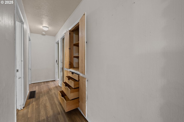 hallway featuring visible vents, dark wood-style flooring, and a textured ceiling