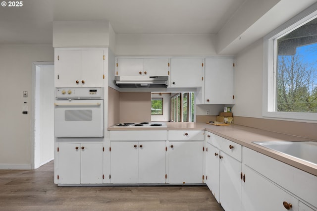 kitchen with under cabinet range hood, white cabinets, white appliances, and wood finished floors