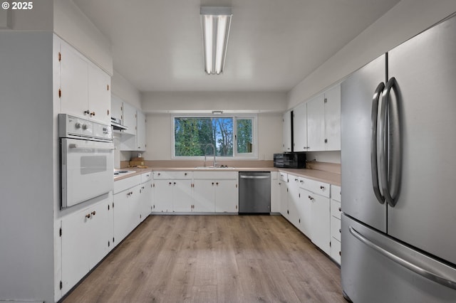 kitchen with a sink, stainless steel appliances, light countertops, white cabinets, and light wood-style floors