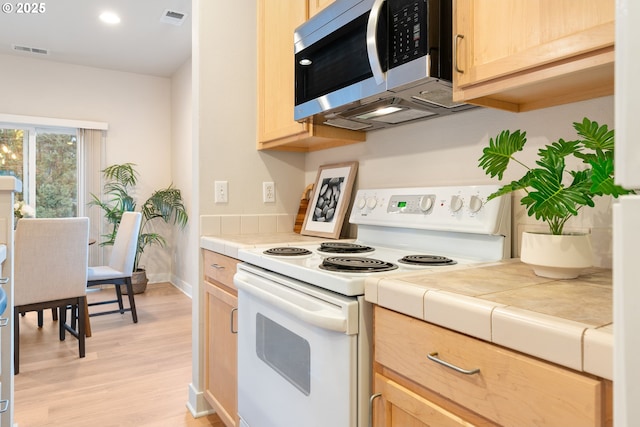 kitchen featuring tile countertops, light brown cabinetry, light hardwood / wood-style floors, and electric range