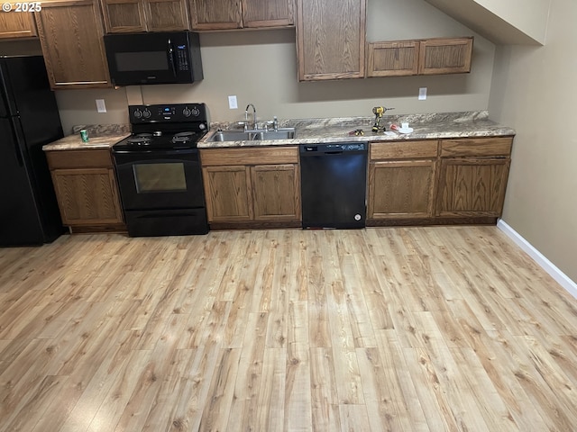 kitchen with light stone countertops, sink, light wood-type flooring, and black appliances