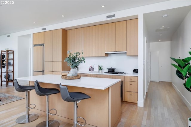 kitchen with light hardwood / wood-style flooring, light brown cabinets, a breakfast bar, and a kitchen island