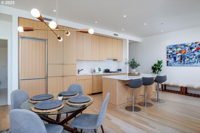 kitchen featuring a kitchen island, light brown cabinetry, sink, paneled built in refrigerator, and light wood-type flooring