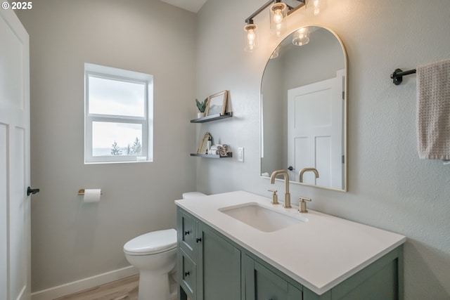 bathroom featuring toilet, baseboards, wood finished floors, and vanity