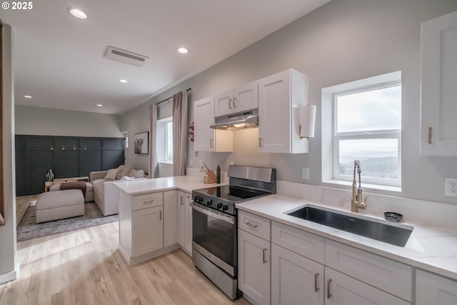 kitchen featuring white cabinets, open floor plan, under cabinet range hood, stainless steel range with electric stovetop, and a sink