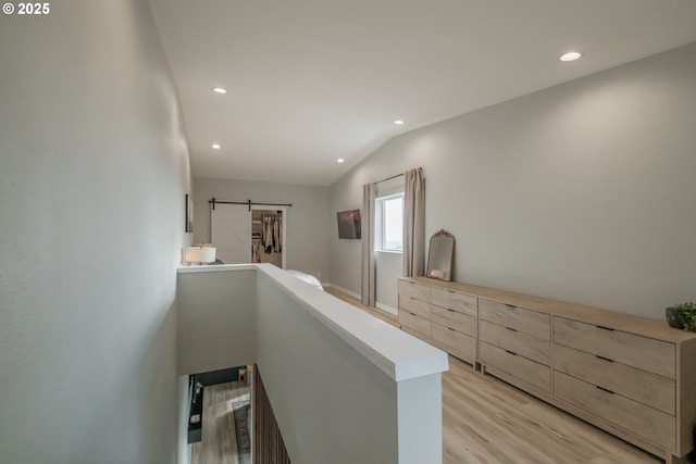 corridor with a barn door, light wood-style flooring, an upstairs landing, and recessed lighting