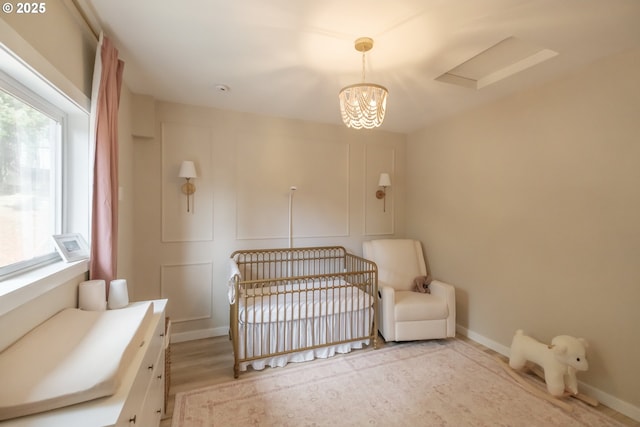 bedroom featuring a nursery area, baseboards, a chandelier, and a decorative wall