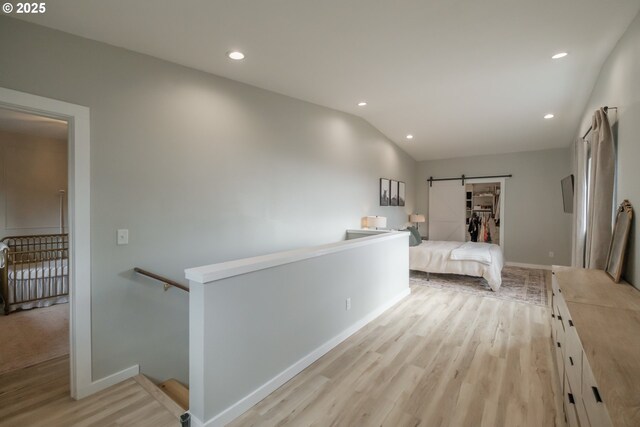 unfurnished bedroom with light wood-type flooring, a barn door, vaulted ceiling, and recessed lighting