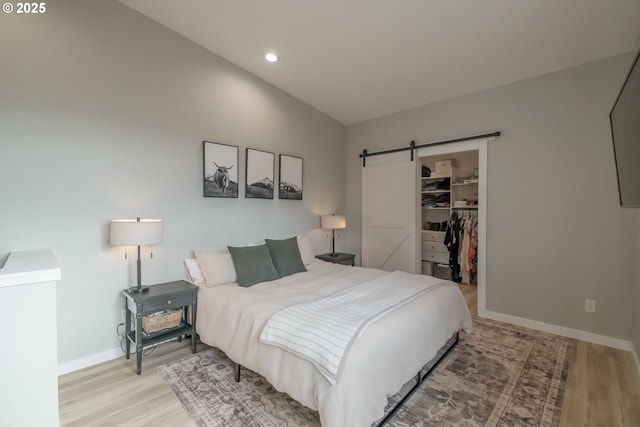 bedroom featuring light wood finished floors, a barn door, baseboards, a spacious closet, and a closet