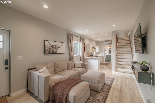 living area featuring stairs, an AC wall unit, light wood-style flooring, and recessed lighting