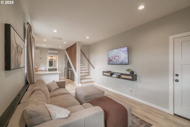 living room featuring light wood finished floors, baseboards, a wall unit AC, stairway, and recessed lighting