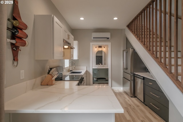 kitchen with light stone counters, white cabinets, a sink, a peninsula, and under cabinet range hood