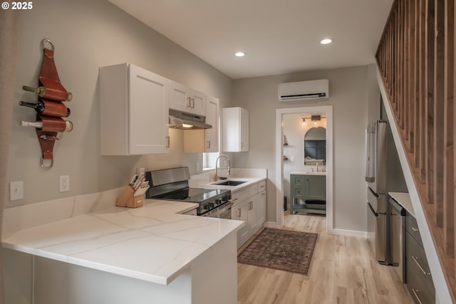 kitchen with stainless steel appliances, a peninsula, a wall unit AC, and white cabinetry