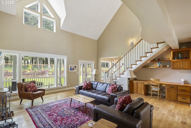 living area with high vaulted ceiling, stairs, and light wood-style flooring