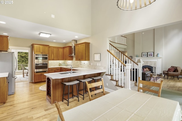 kitchen with appliances with stainless steel finishes, a peninsula, light wood-style floors, brown cabinetry, and tasteful backsplash
