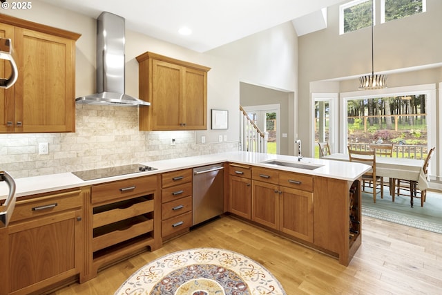 kitchen featuring wall chimney range hood, a sink, dishwasher, light countertops, and a peninsula