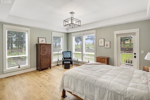 bedroom featuring light wood-type flooring, a raised ceiling, access to exterior, and a chandelier