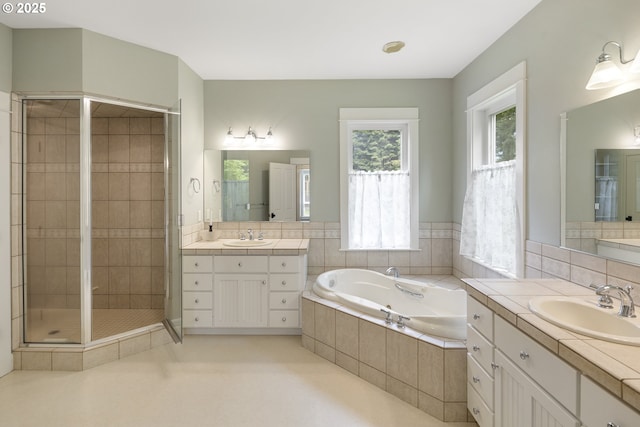 bathroom with a garden tub, a stall shower, and two vanities