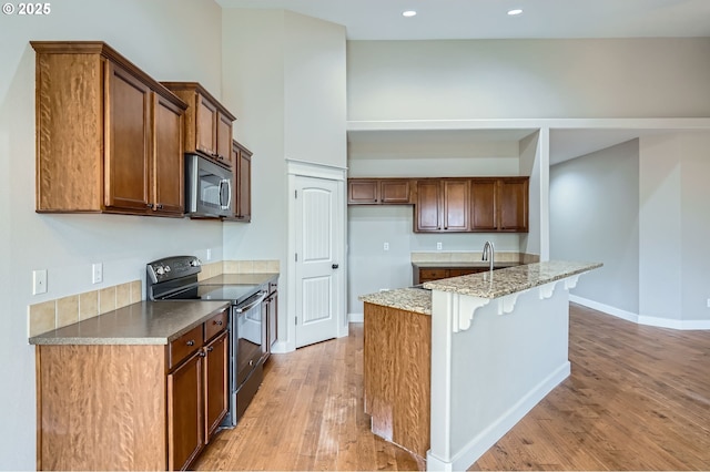 1080 Sage St, Silverton, OR 97381 - kitchen with black range with electric cooktop, stainless steel microwave, light wood-type flooring, a kitchen island with sink, and brown cabinetry