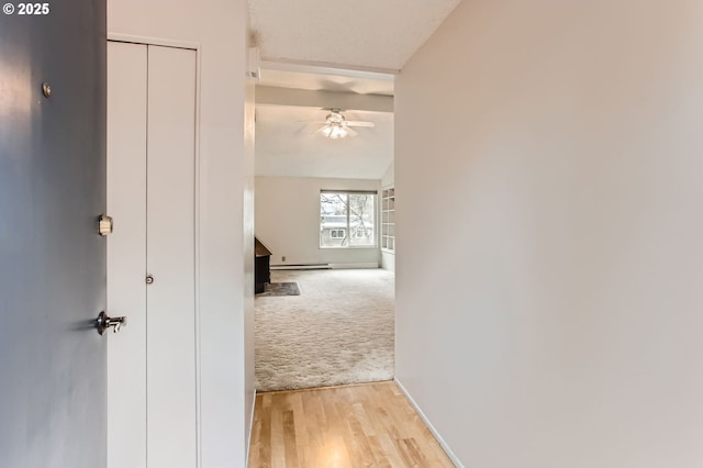 hallway with light colored carpet, a baseboard heating unit, light wood-style floors, vaulted ceiling, and baseboards