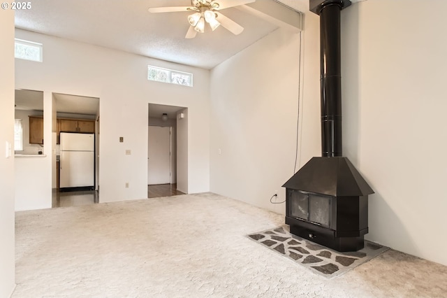 unfurnished living room with a ceiling fan, carpet, and a wood stove