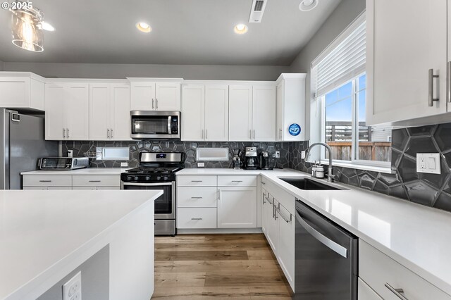 kitchen featuring appliances with stainless steel finishes, white cabinetry, hanging light fixtures, a center island, and light hardwood / wood-style flooring