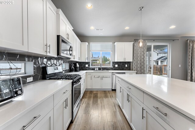 kitchen with sink, white cabinets, backsplash, stainless steel appliances, and light hardwood / wood-style flooring