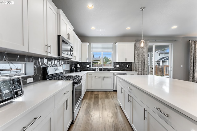 kitchen with sink, white cabinetry, tasteful backsplash, hanging light fixtures, and appliances with stainless steel finishes