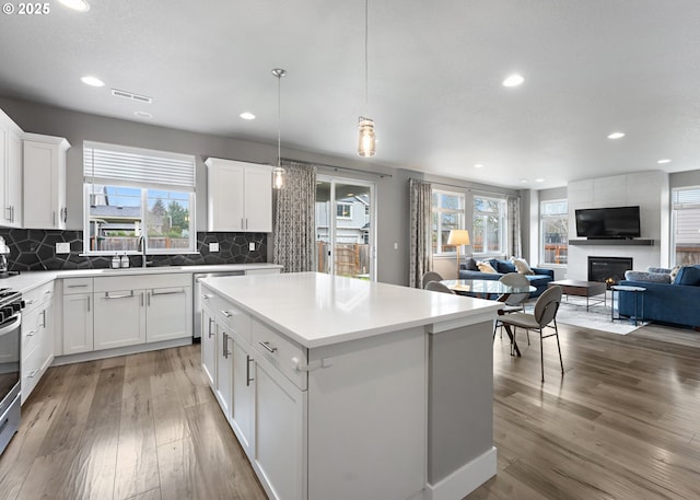 kitchen featuring pendant lighting, white cabinetry, wood-type flooring, a large fireplace, and a kitchen island