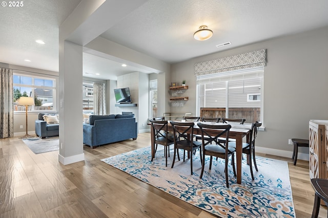 dining room featuring a textured ceiling, light wood finished floors, visible vents, and baseboards