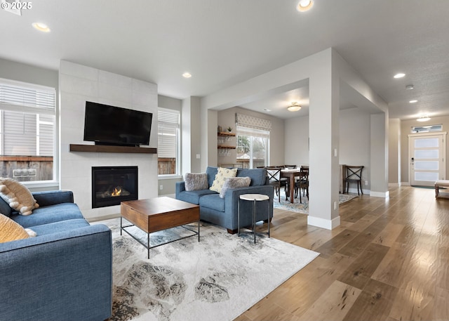 living room featuring baseboards, a tiled fireplace, wood finished floors, and recessed lighting