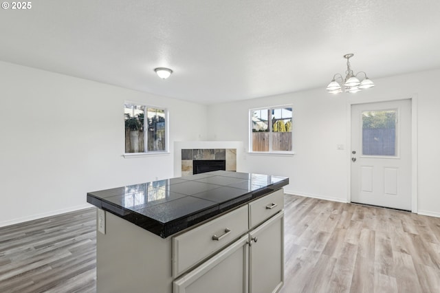 kitchen featuring hanging light fixtures, white cabinets, a kitchen island, light hardwood / wood-style flooring, and a tiled fireplace