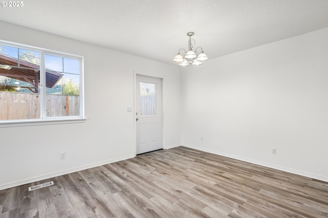 empty room featuring a wealth of natural light, light hardwood / wood-style flooring, and a chandelier