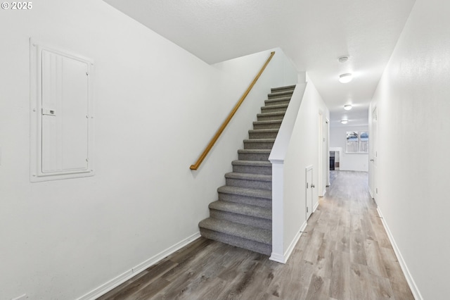 stairway with hardwood / wood-style floors and electric panel