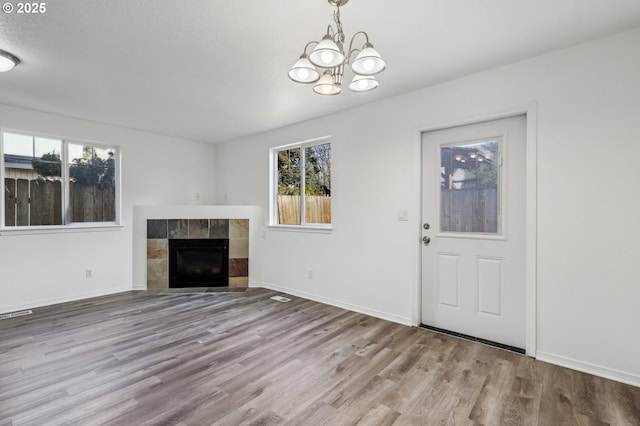 unfurnished living room with a tile fireplace, a notable chandelier, and light wood-type flooring